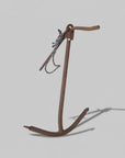 A rusted metal anchor with a chain, photographed on a concrete floor.