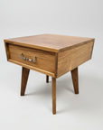 A sleek mid century modern end table made from solid wood with a visible drawer, finished in a windswept texture, placed against a white background.