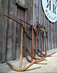 Rusty metal anchor-like props leaning against a weathered wooden building wall, with a round white sign reading 'Rustic To Refined' and a storefront entrance in the background.