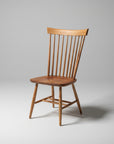 A wooden Shaker chair with a smooth finish and simple design, featuring a scooped seat and vertical spindles on the backrest.