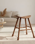 Wooden stool with a curved seat and four legs on a textured surface.