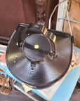 A vintage black metal lantern or light fixture photographed from above, resting on a blue surface in a cluttered indoor setting with books and wooden furniture visible.