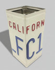 A vintage-style metal tin canister designed to look like a California license plate, featuring the word 'CALIFORNIA' in red letters and the plate number 'FC1' in blue on an off-white background, set against a solid gray backdrop.