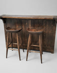 A rustic Century Split Level Bar made of solid wood, featuring a counter, two bar stools, drawers, shelves, and a wine rack.