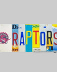 A custom license plate sign featuring the word 'RAPTORS' in vibrant colors on a wooden background with a logo and text.