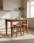 A rectangular Shaker style harvest table made of wood with tapered legs, accompanied by two wooden stools.