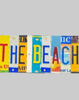A custom license plate sign made from repurposed license plates, mounted on painted wood with the text 'THE BEACH' arranged in a visually appealing way.