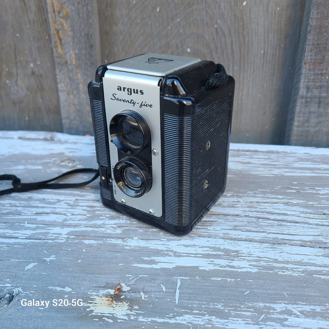 A vintage Argus S-20 Super 16 film camera with a black ribbed body and silver front plate, resting on a weathered, peeling blue-gray wooden surface.
