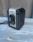 A vintage Argus S-20 Super 16 film camera with a black ribbed body and silver front plate, resting on a weathered, peeling blue-gray wooden surface.