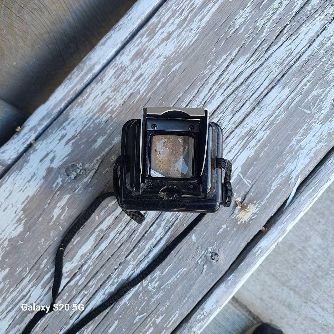 A vintage black instant camera with a strap, resting on a weathered, peeling white wooden deck. 