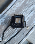 A vintage black instant camera with a strap, resting on a weathered, peeling white wooden deck. 
