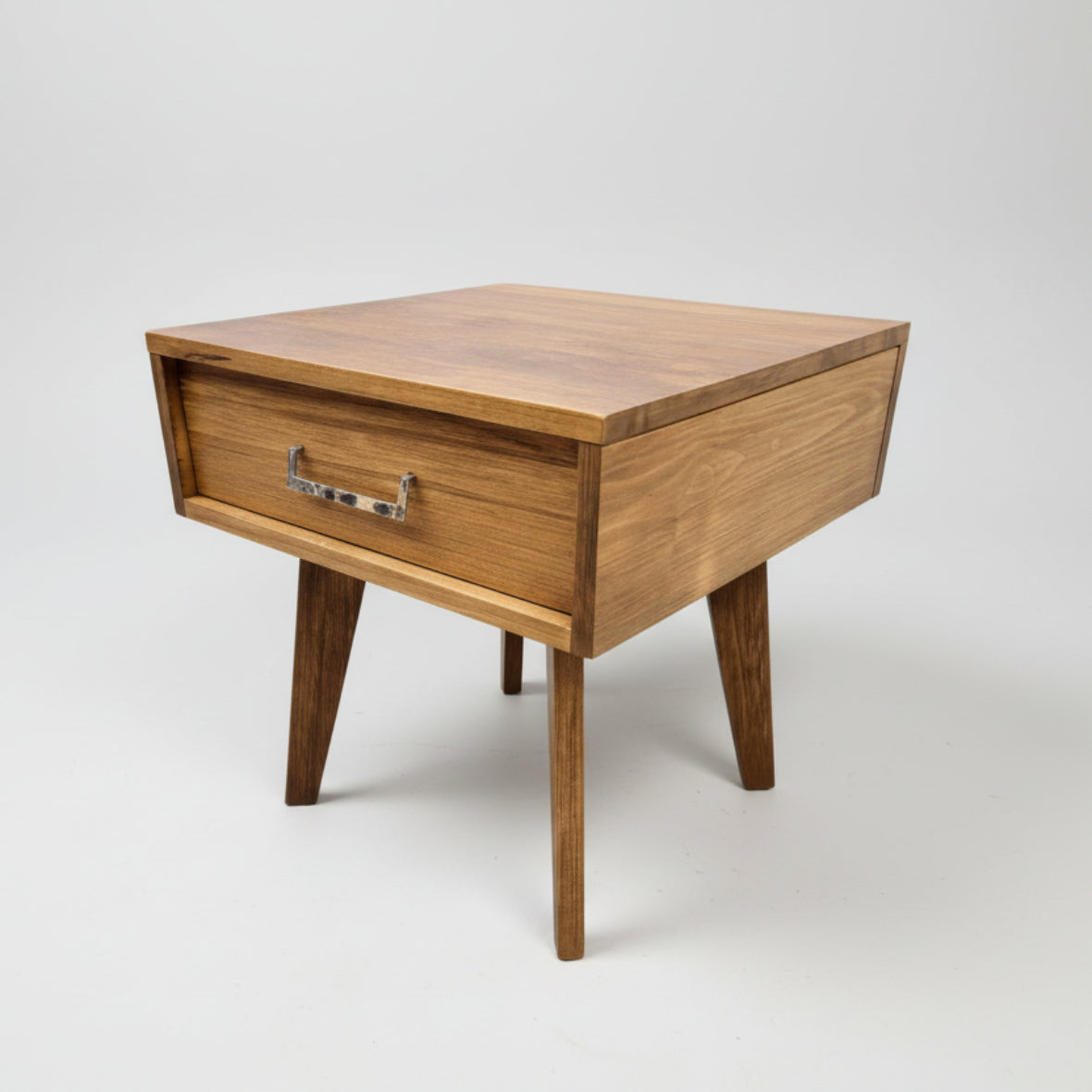 A sleek mid century modern end table made from solid wood with a visible drawer, finished in a windswept texture, placed against a white background.