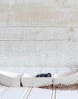 White ceramic canoe bowl with blueberries on a wooden surface.