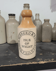 Vintage stoneware bottle with 'Gould, Hibberd & Randall Ltd,  Isle of Wight Ltd' label among other bottles on a table.