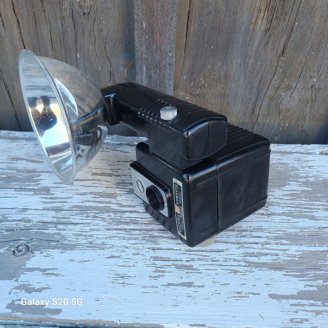 A vintage black wall-mounted camera with a silver dome reflector, photographed resting on weathered wooden boards.