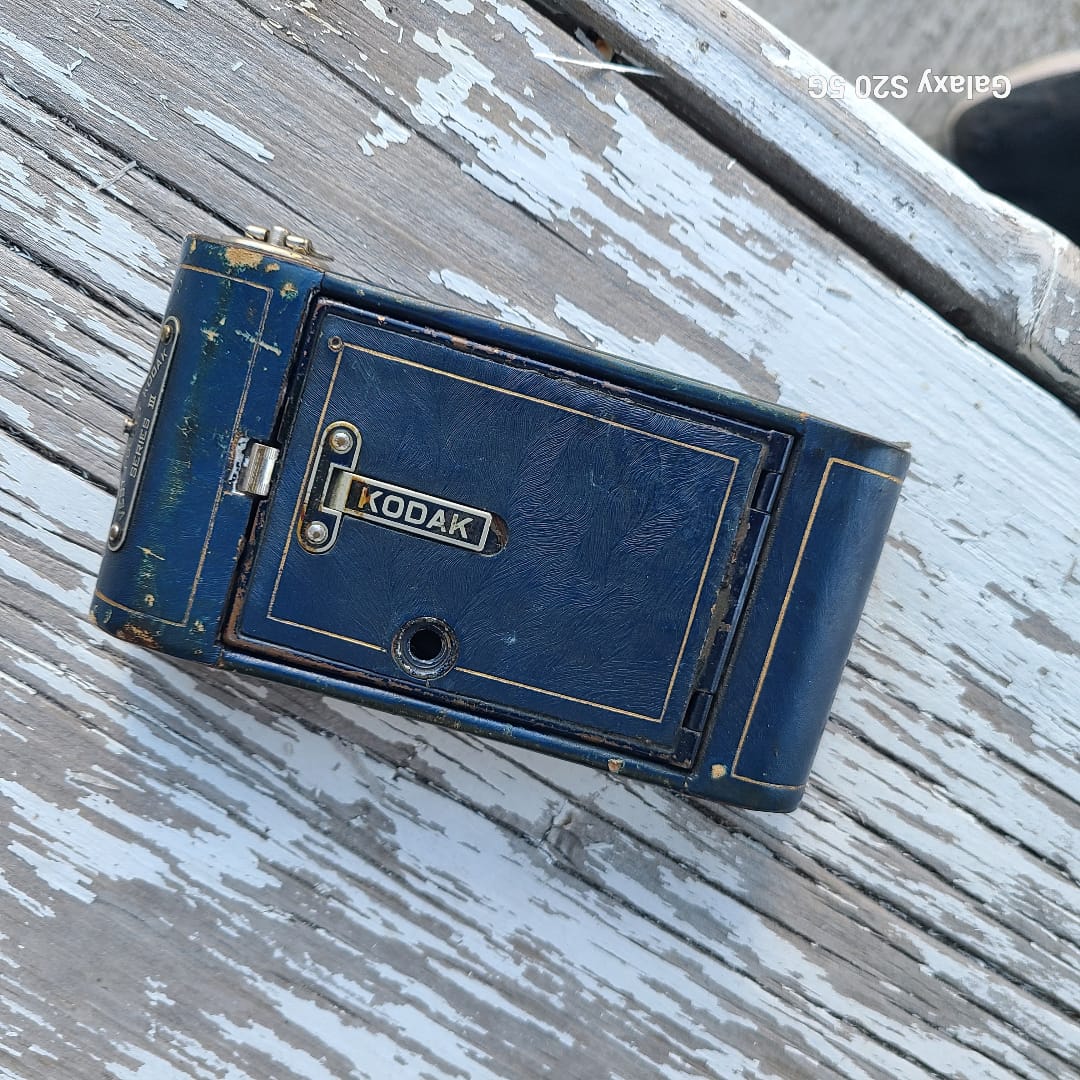 A vintage blue Kodak camera body resting on a weathered, white-painted wooden surface.