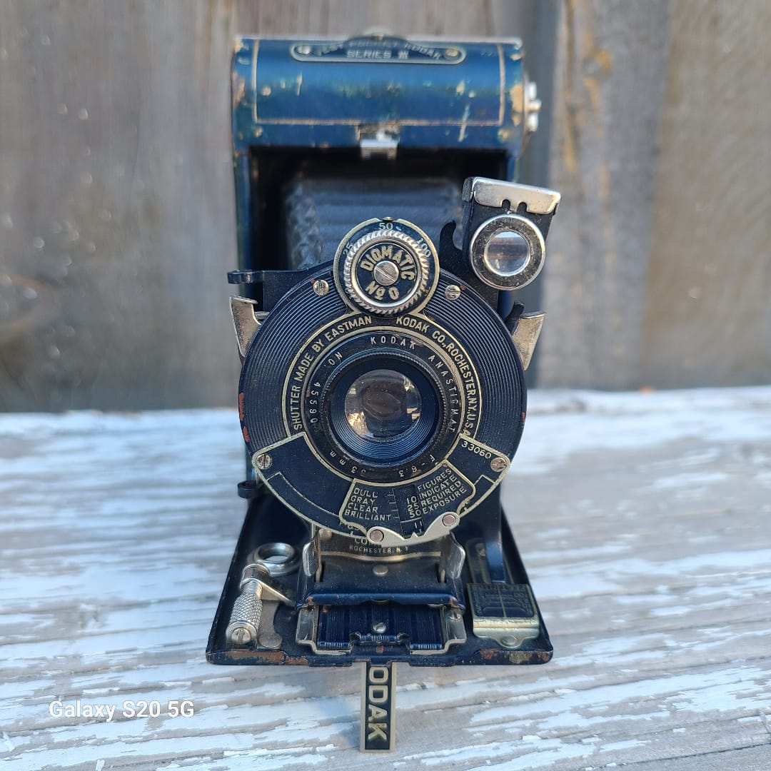 Vintage black and blue Kodak Portra 400 SLR camera shown from the front, resting on a weathered white-painted wooden surface.