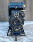 Vintage black and blue Kodak Portra 400 SLR camera shown from the front, resting on a weathered white-painted wooden surface.