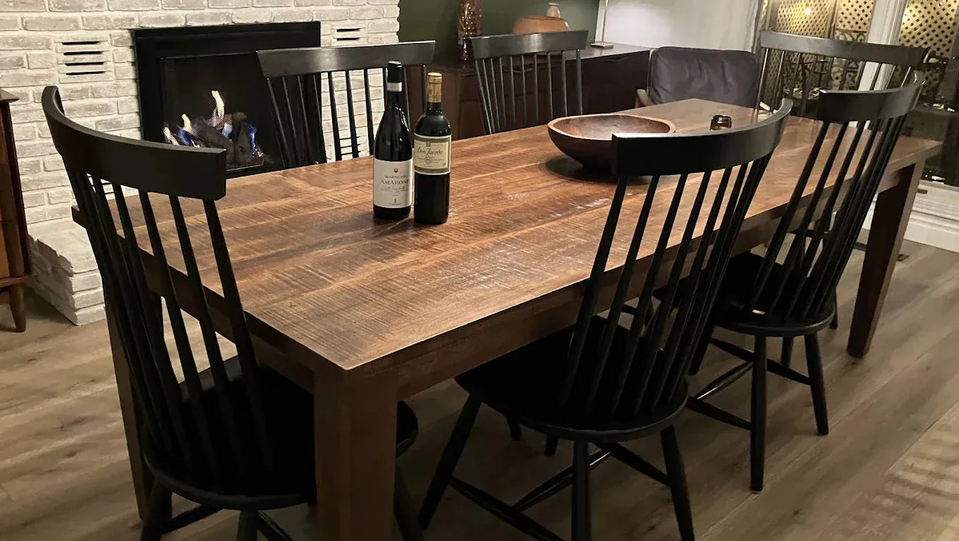 Wooden dining table with black chairs and wine bottles in a cozy room.