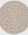 A round, hand-made knotted trivet in a light oatmeal beige color, shown from a top-down view against a neutral light gray background.