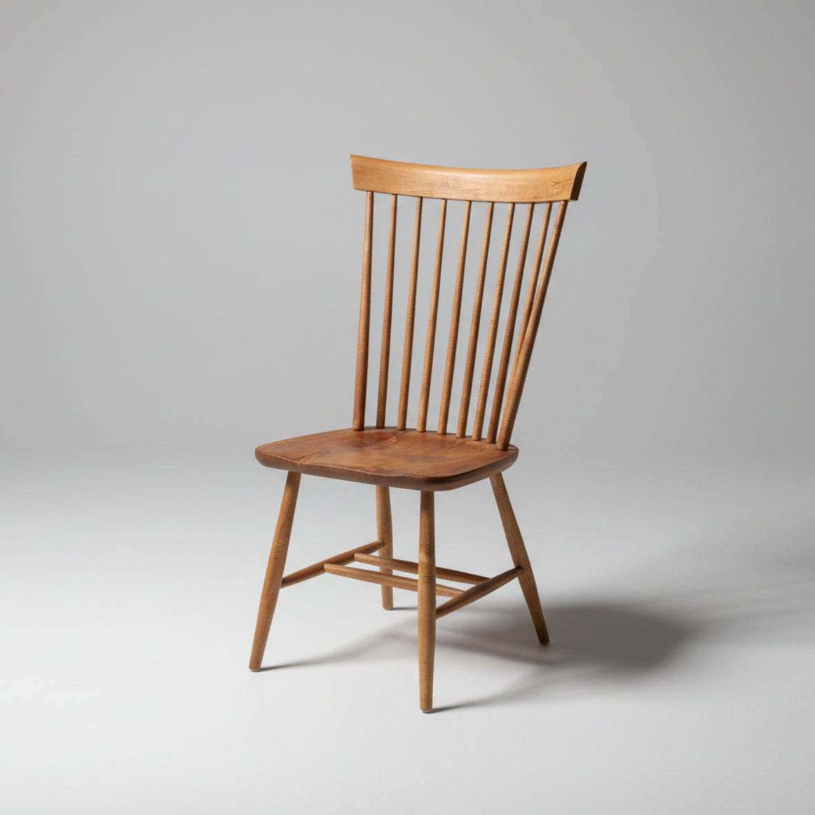 A wooden Shaker chair with a smooth finish and simple design, featuring a scooped seat and vertical spindles on the backrest.