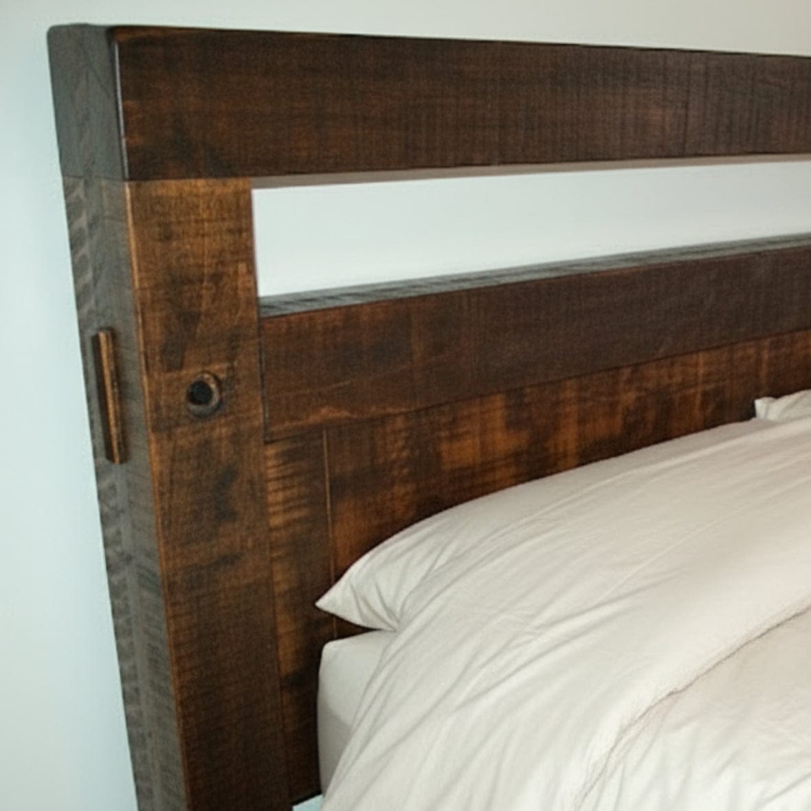 Wooden headboard with white bedding against a plain wall