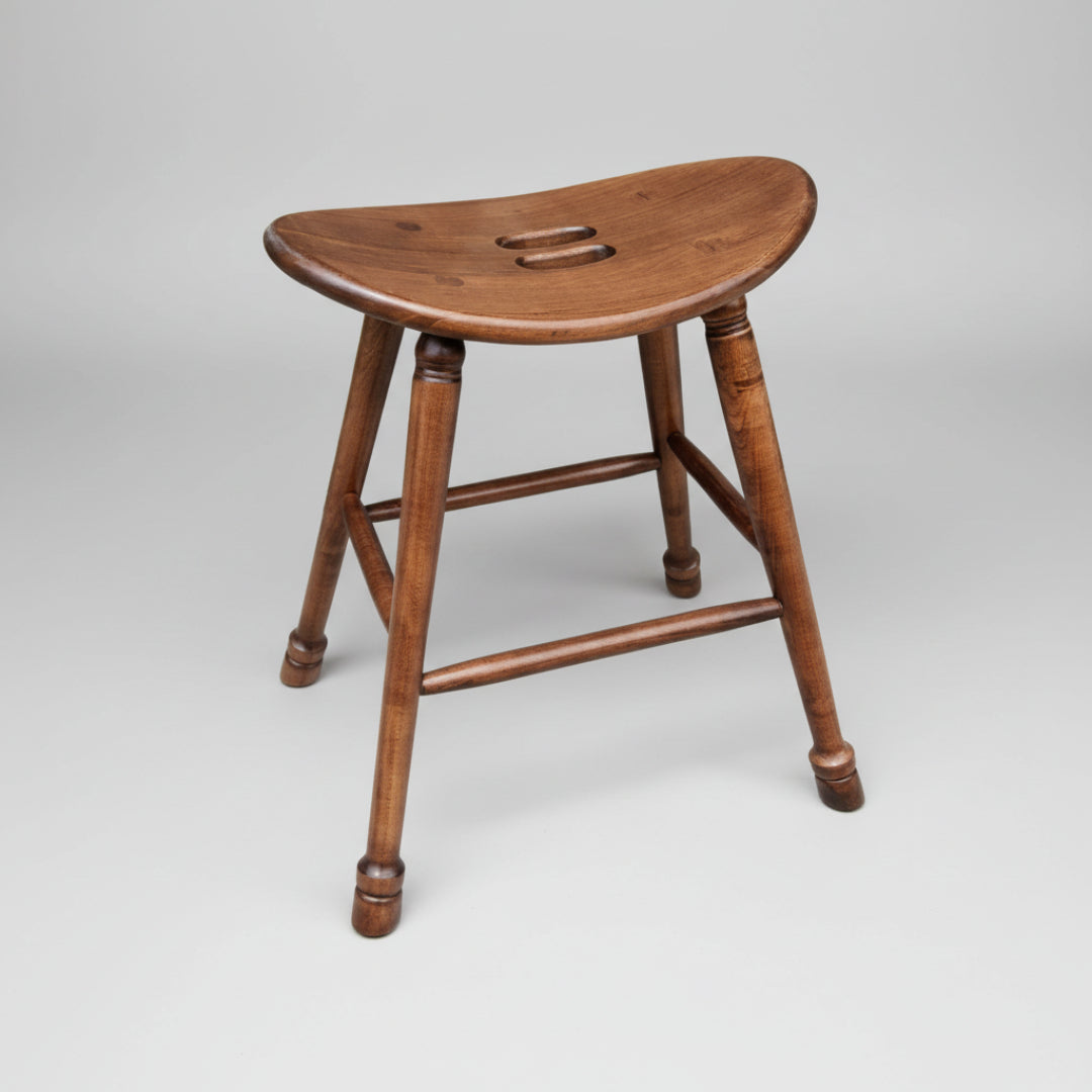 A wooden saddle stool with a smooth finish and turned leg, featuring a grab hole in the seat for easy mobility.