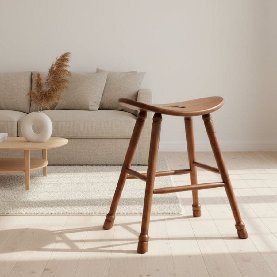 Wooden stool with a curved seat and four legs on a textured surface.