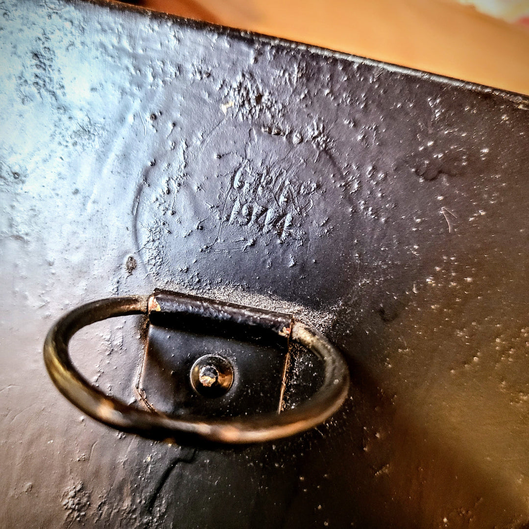 Close-up of a dark cast iron or metal surface with a small oval handle and embossed text reading 'Crazy 1972'.