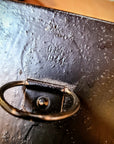 Close-up of a dark cast iron or metal surface with a small oval handle and embossed text reading 'Crazy 1972'.