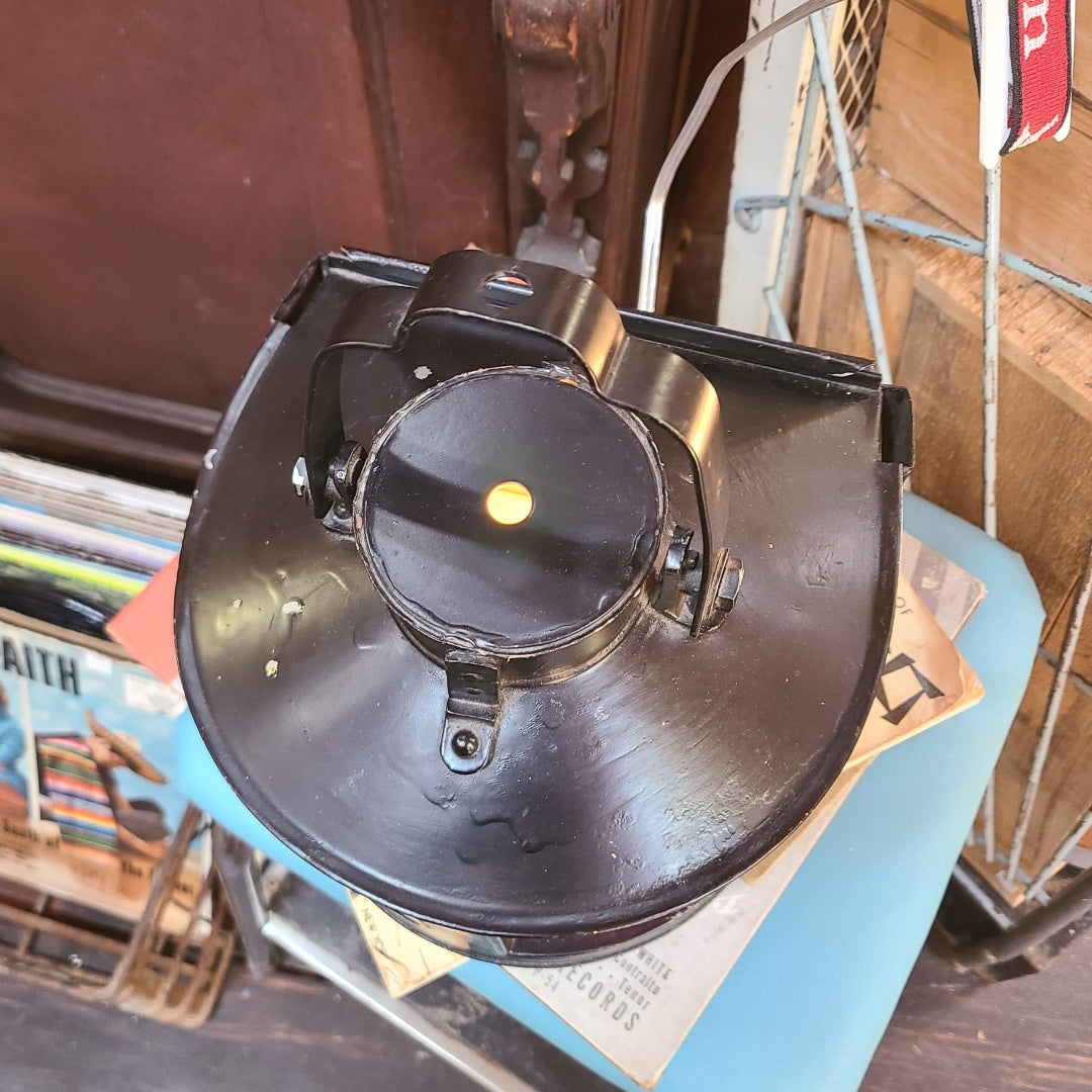 A vintage black metal lantern or light fixture photographed from above, resting on a blue surface in a cluttered indoor setting with books and wooden furniture visible.