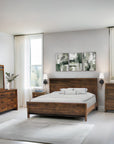 Wooden bedroom furniture set with bed, dressers, and mirror in a bright room.