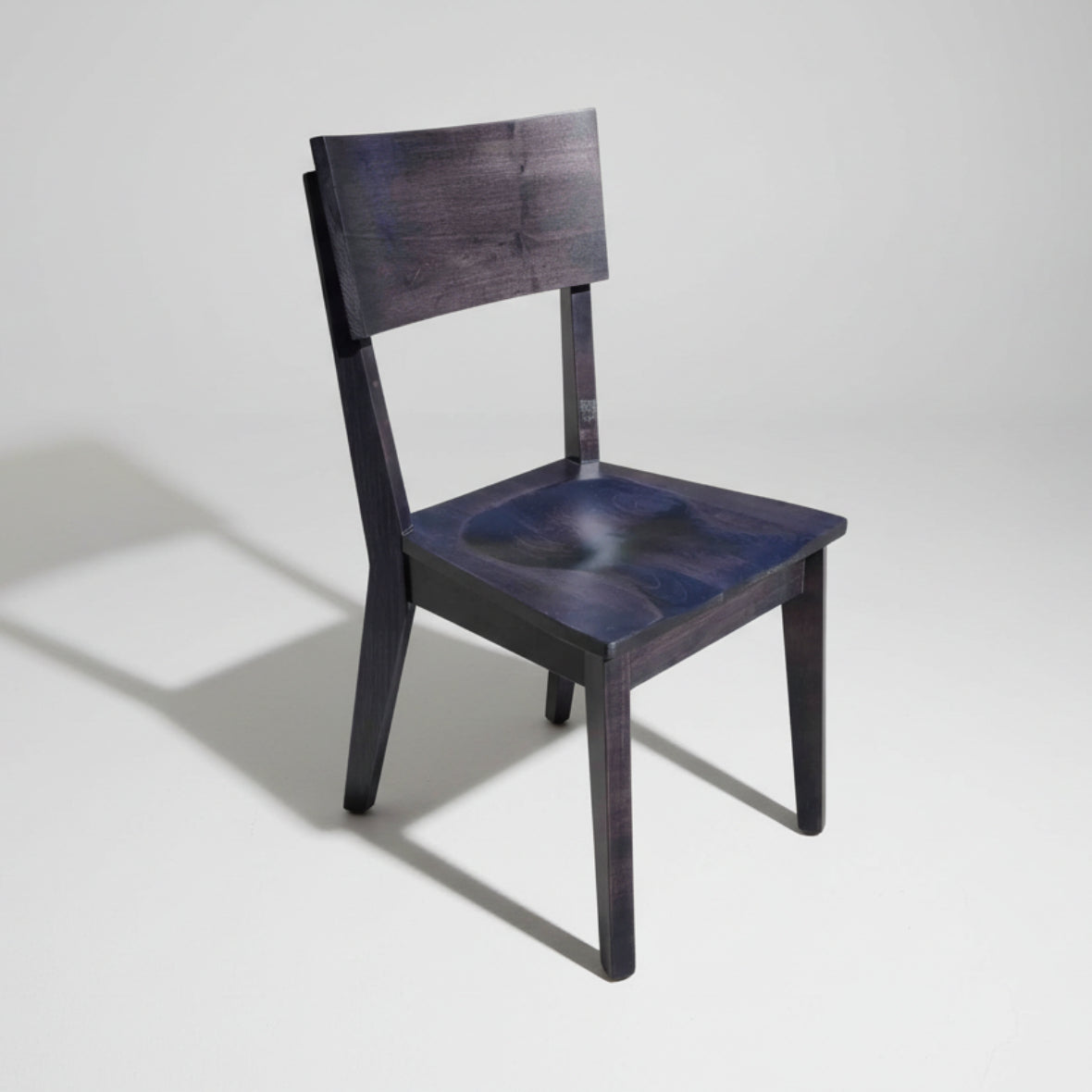 A sleek mid century modern dining chair with solid wood construction, handcrafted in Canada. The chair has a dark wood texture with a flat backrest and a seat.