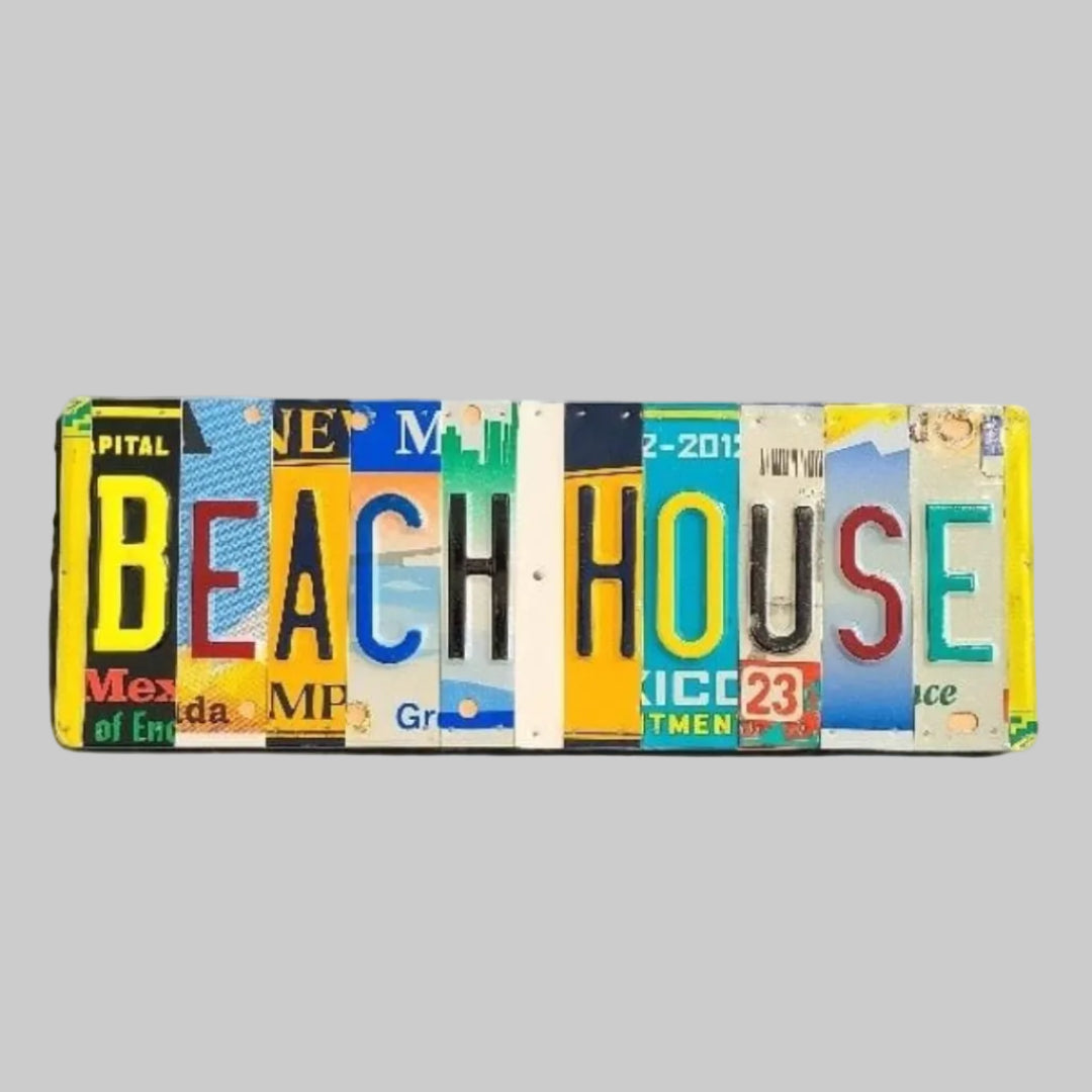A custom license plate sign made from repurposed plates, mounted on painted wood with a variety of colorful text and graphics, spelling out 'BEACH HOUSE'.