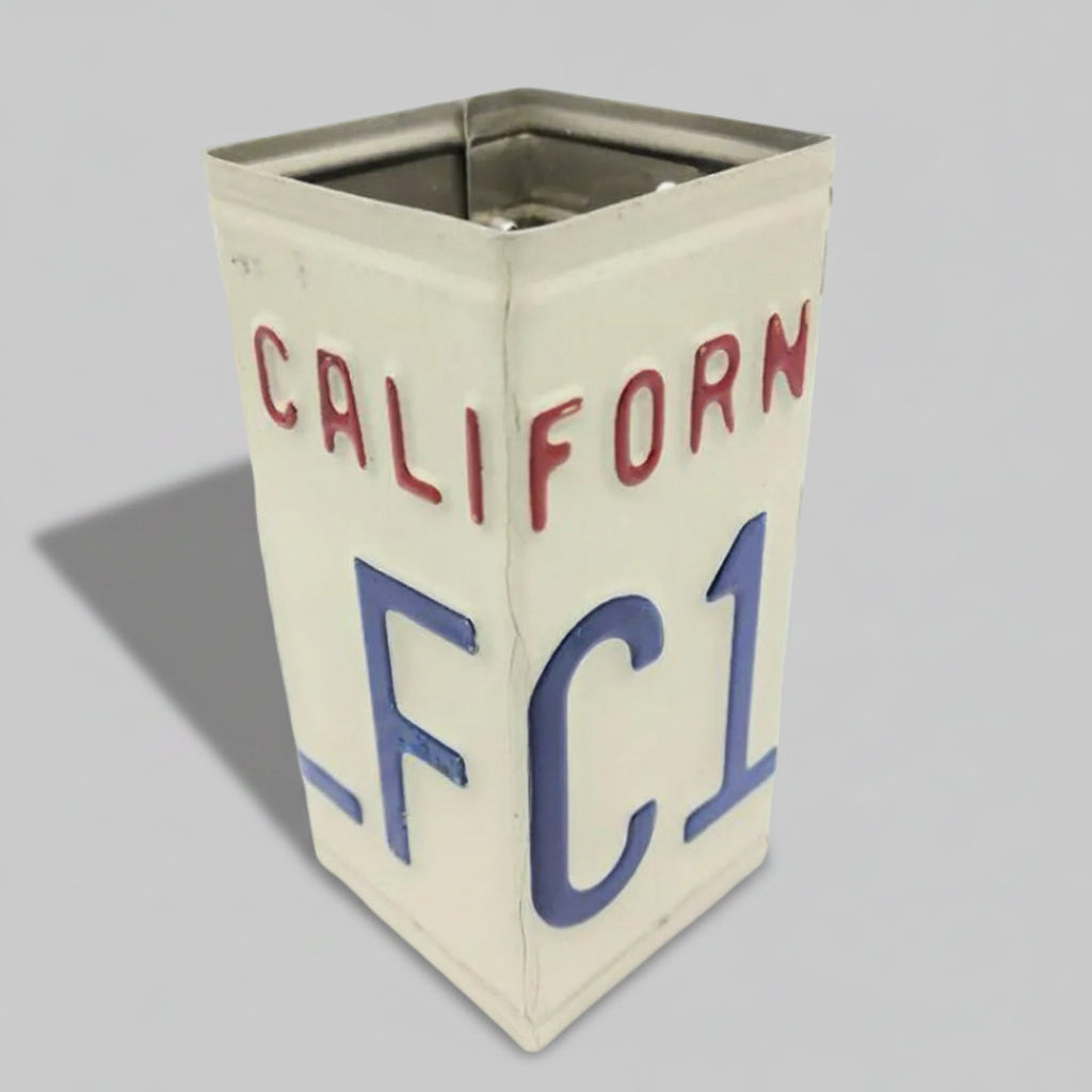 A vintage-style metal tin canister designed to look like a California license plate, featuring the word 'CALIFORNIA' in red letters and the plate number 'FC1' in blue on an off-white background, set against a solid gray backdrop.
