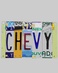 A custom license plate sign made from repurposed license plates, mounted on painted wood with various colors and text, including 'CHEVY' and 'THE OTHER GUY'.