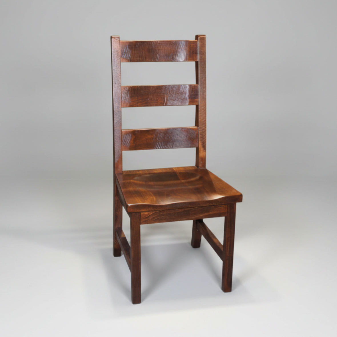 A rustic Dakota ladder back side chair made of solid wood, with a visible wood grain and saw marks, standing against a white background.