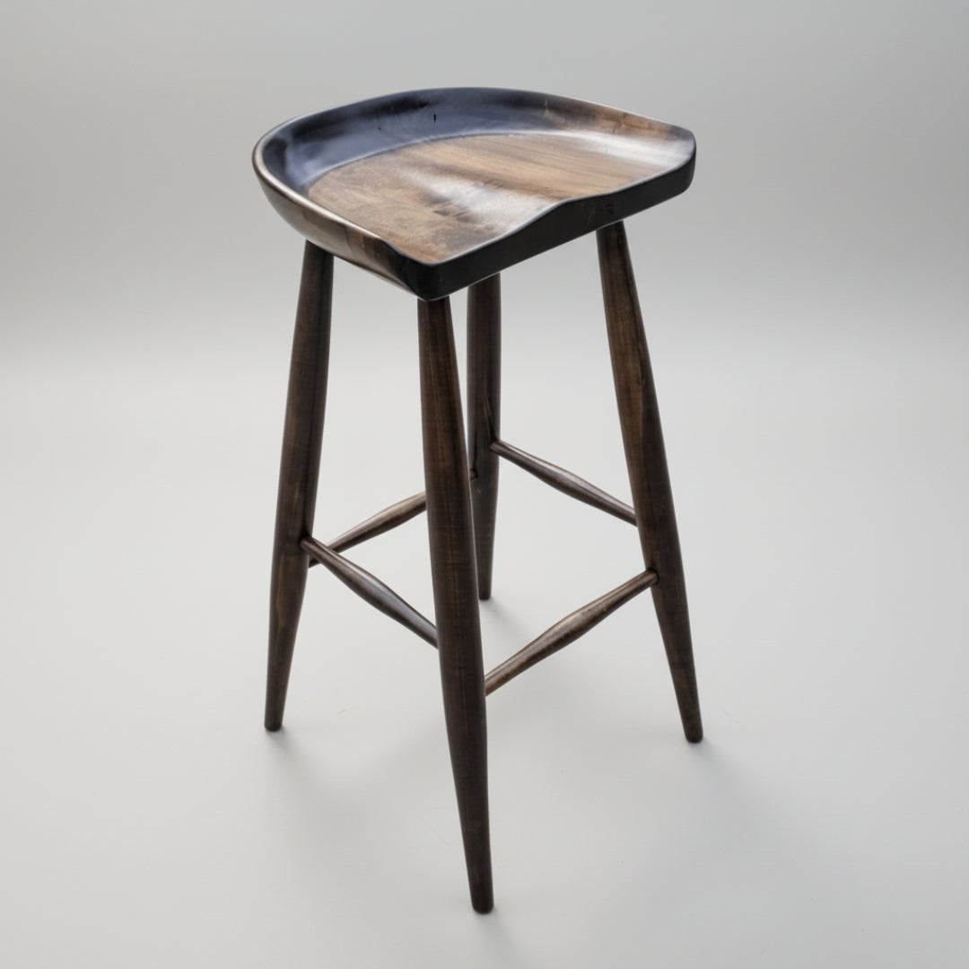 A brown wooden stool with a unique seat scoop design, featuring a smooth wood texture and a flat base. The stool has a modern aesthetic with a dark grain finish.