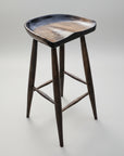 A brown wooden stool with a unique seat scoop design, featuring a smooth wood texture and a flat base. The stool has a modern aesthetic with a dark grain finish.