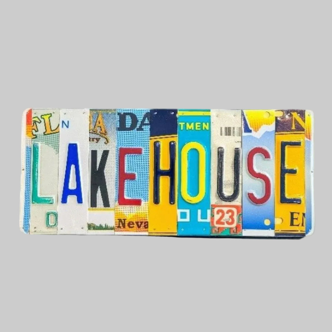 A custom license plate sign made from repurposed license plates, mounted on a wooden board with a colorful array of plates featuring various text and graphics, and the word 'LAKEHOUSE' prominently displayed.
