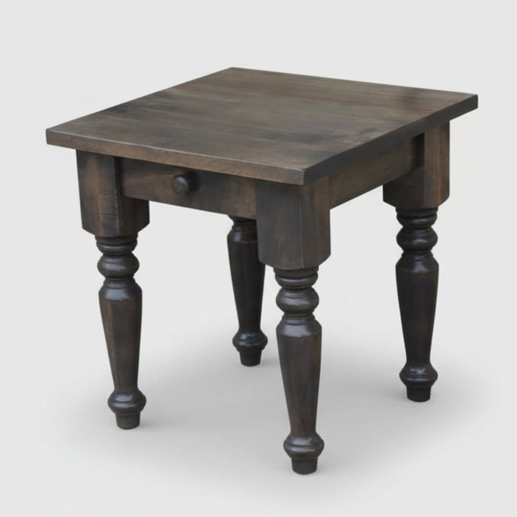 A rustic wooden end table with handcrafted turned legs and a drawer, made from solid wood.