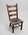 A rustic ladder chair made of solid wood with a seat scoop and a backrest, featuring a natural wood finish.