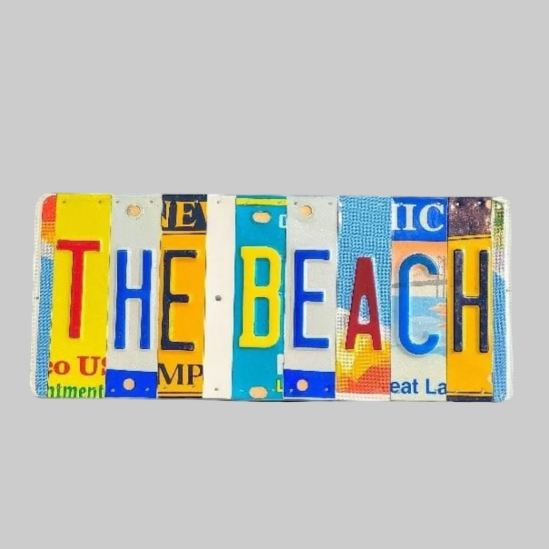 A custom license plate sign made from repurposed license plates, mounted on painted wood with the text 'THE BEACH' arranged in a visually appealing way.